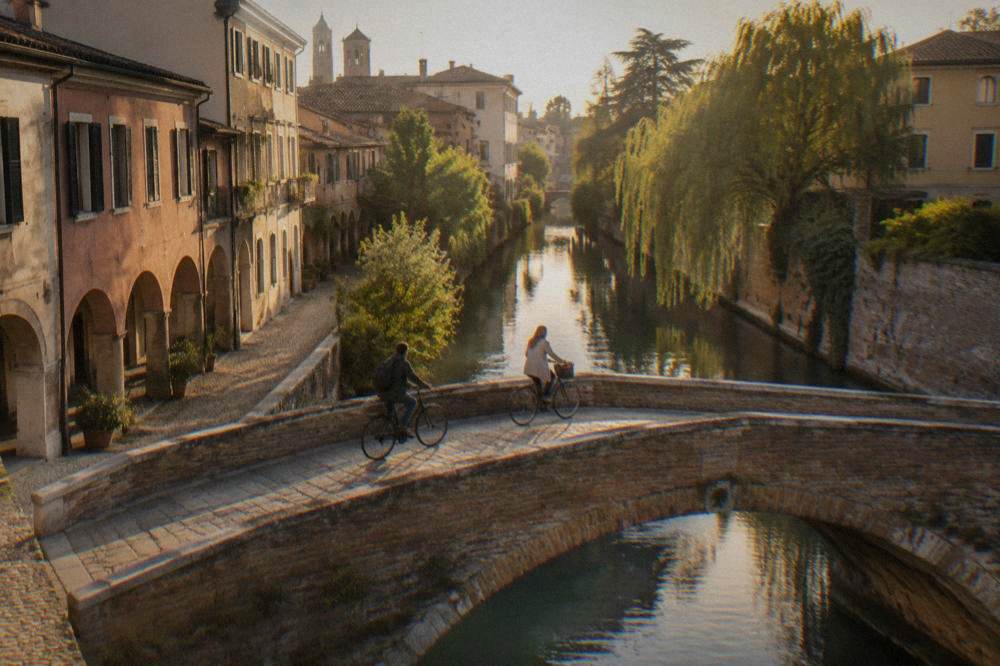 Cyclists crossing a small bridge over a narrow river in a northern Italian town