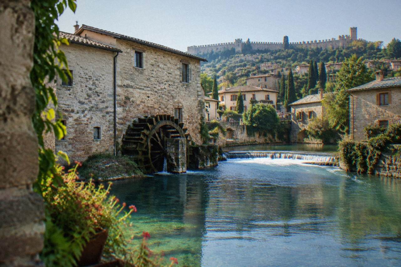 Stone houses and an arched watermill wheel along a quiet river in Borghetto