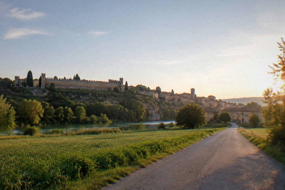 A narrow country road through flat green farmland toward a distant village