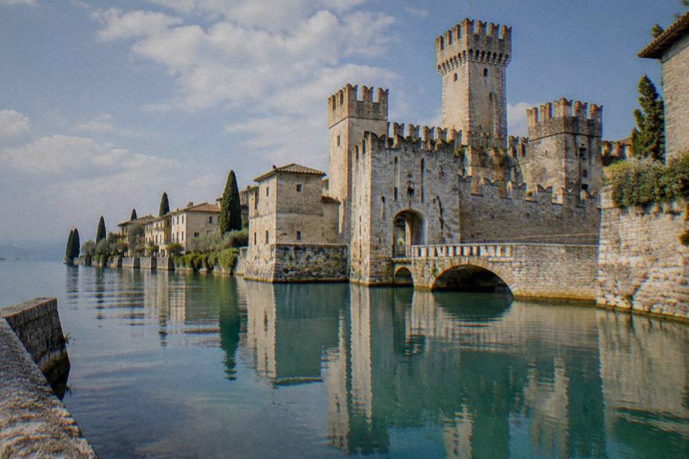 A walled lakeside town with cypress trees reflected in still water at Sirmione