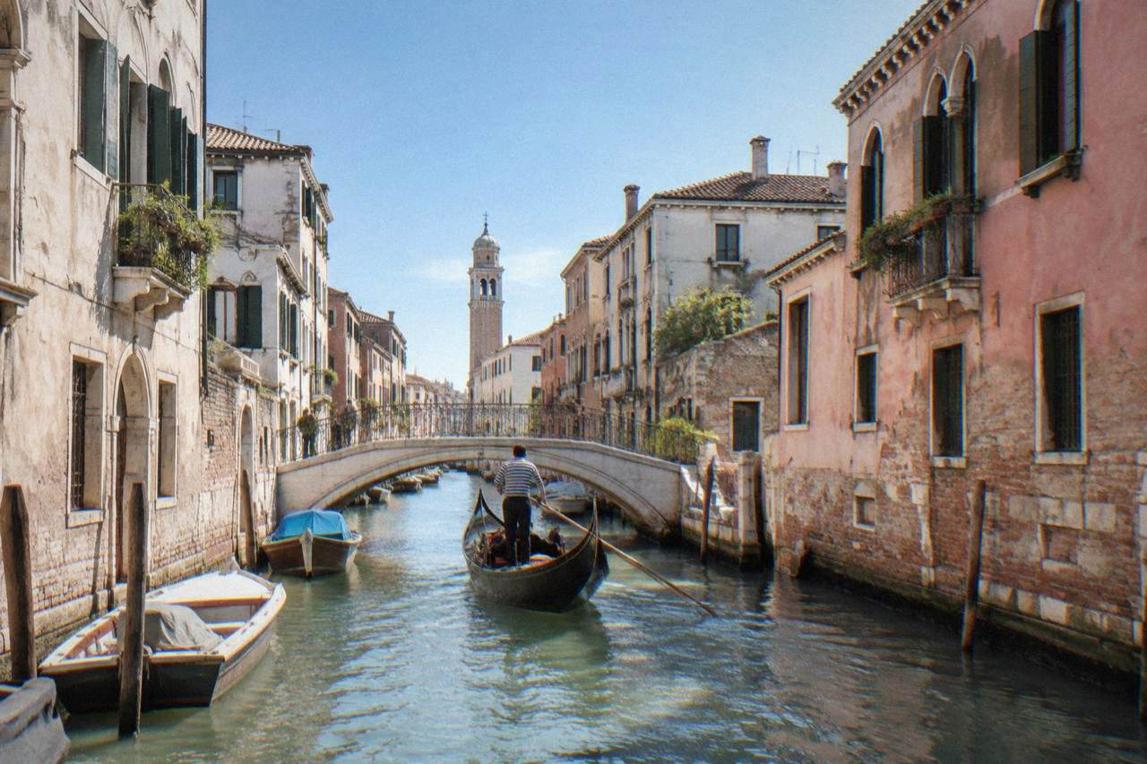 A canal in Venice with a gondola passing under a small stone bridge