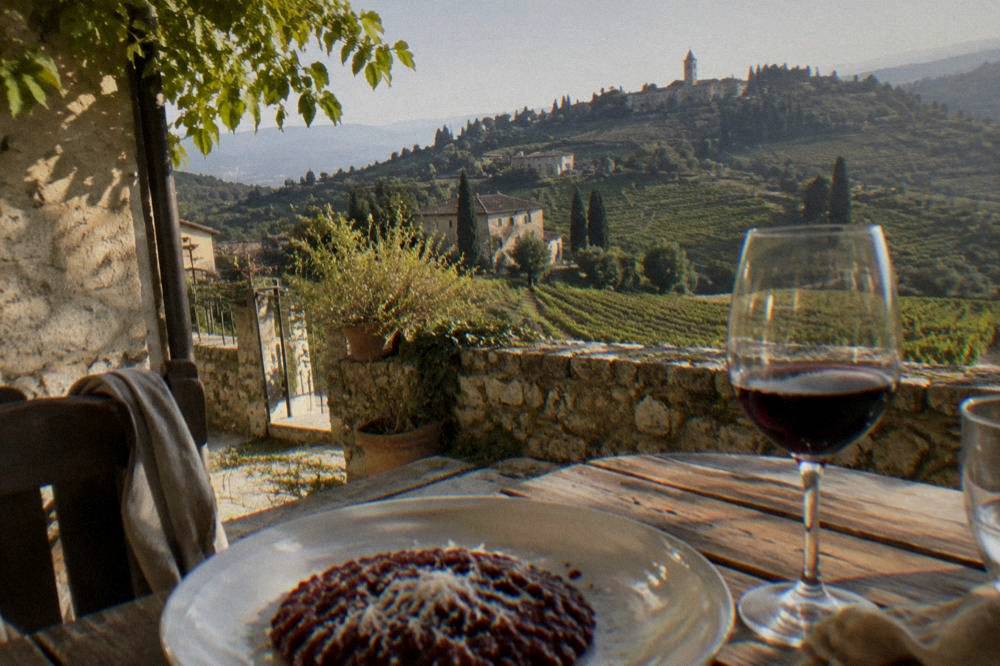 A plate of dark red risotto with grated cheese beside a glass of red wine