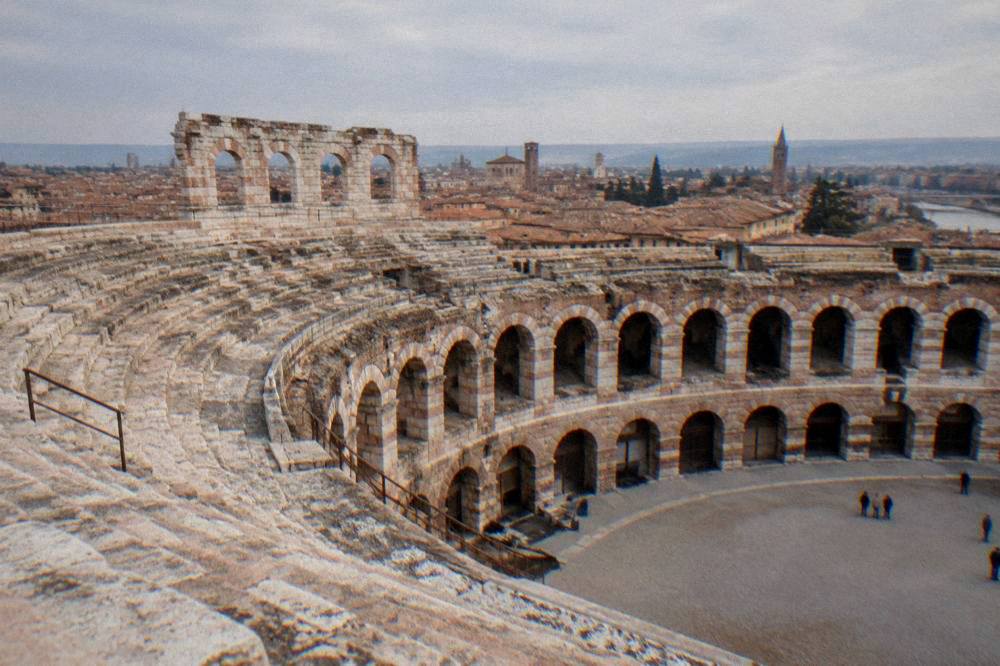 The open top ring of the Verona Arena seen from a high stone seat with rooftops beyond