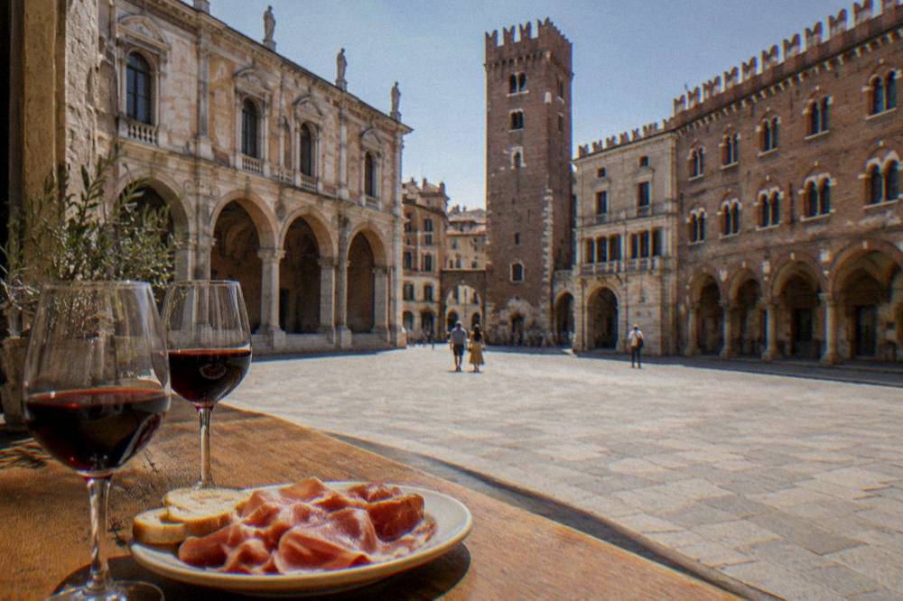 Glasses of red wine on a wooden counter beside a plate of cured meat