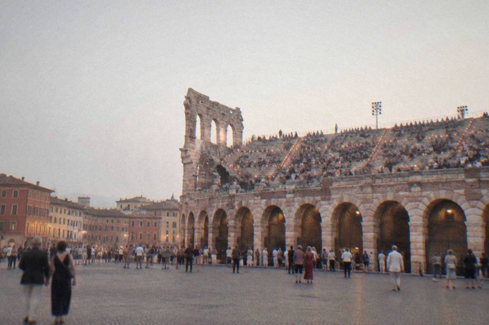 Candle-lit stone steps of the Arena di Verona filling with an opera audience at dusk