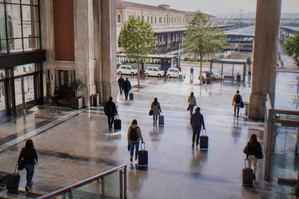 Travellers with suitcases walking through the concourse of an Italian railway station