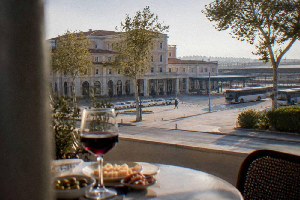 Glass of red wine and small snack plates on a table with a city view behind