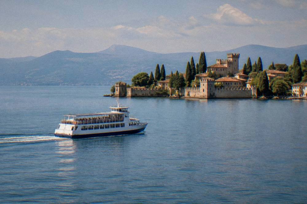 Ferry crossing a large lake towards a walled peninsula town with a castle