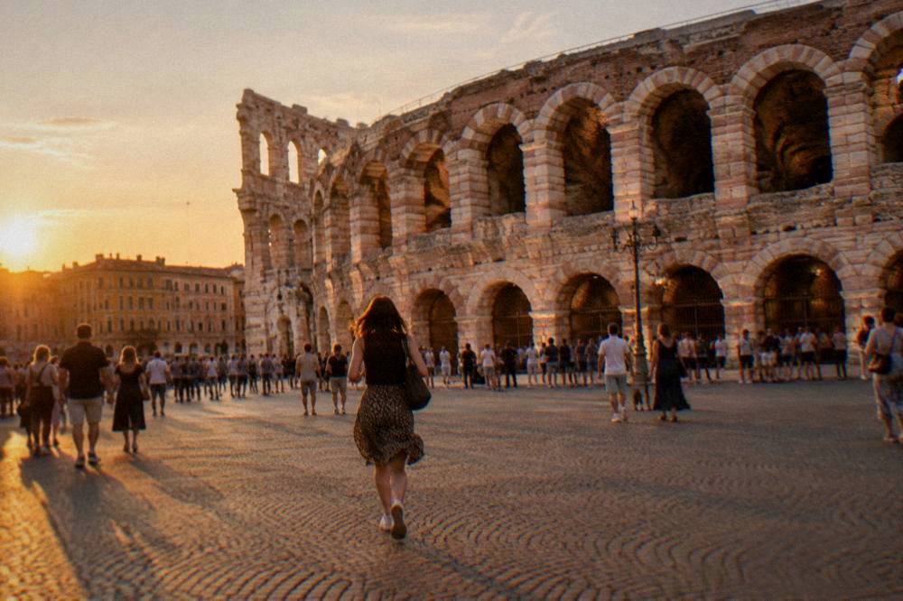 The lit facade of the Verona Arena glowing above evening crowds in Piazza Bra