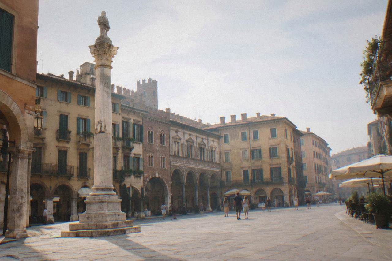 A wide stone square in Verona with old market buildings and a marble column under a soft morning sky