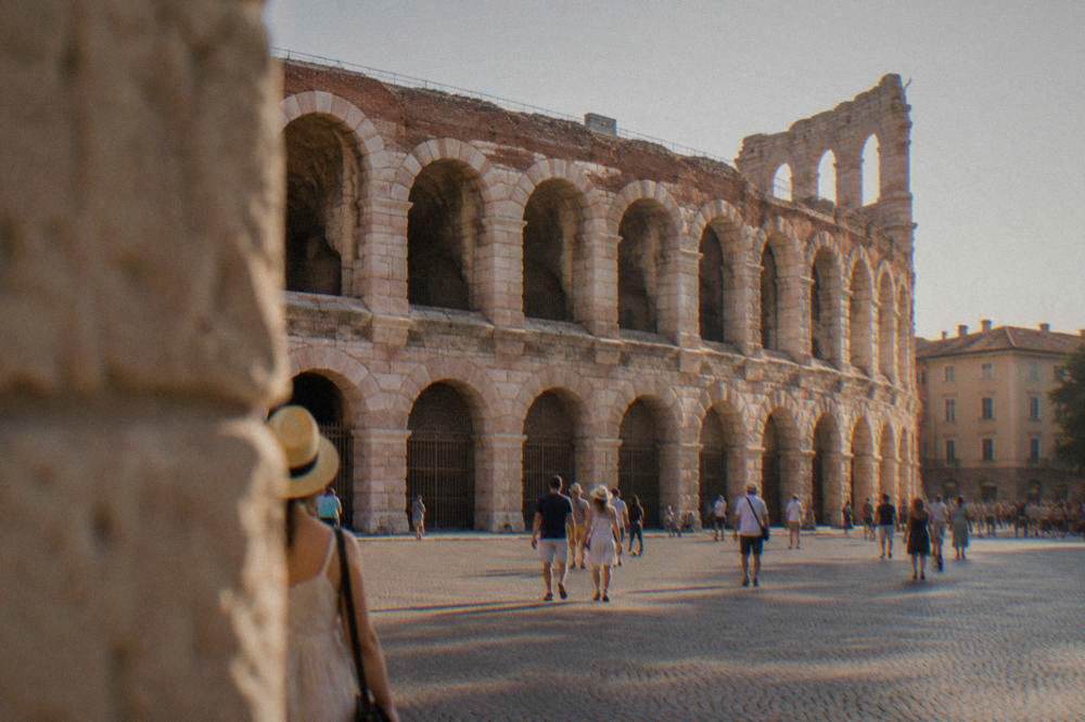 A massive Roman amphitheatre of pink stone seen from a wide open square at golden hour