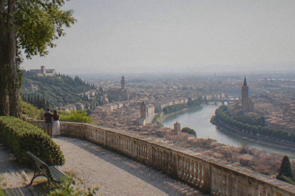 A panoramic view over red rooftops and a curving river from a green hilltop terrace