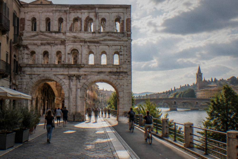 Cyclists riding a path beside the Adige river with Verona's bridges in the background