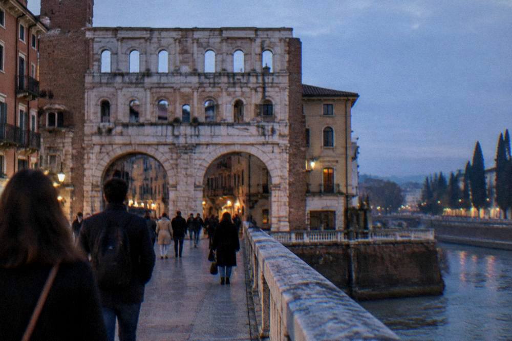 People walking across one of Verona's stone bridges over the Adige at dusk