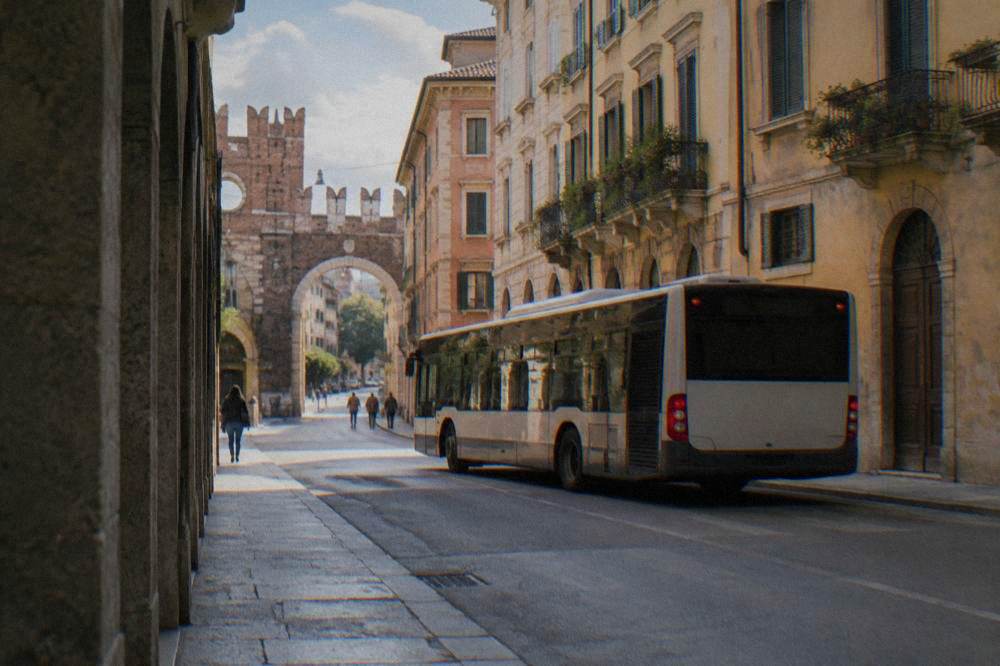 A city bus stopped on a street in Verona beside old stone buildings