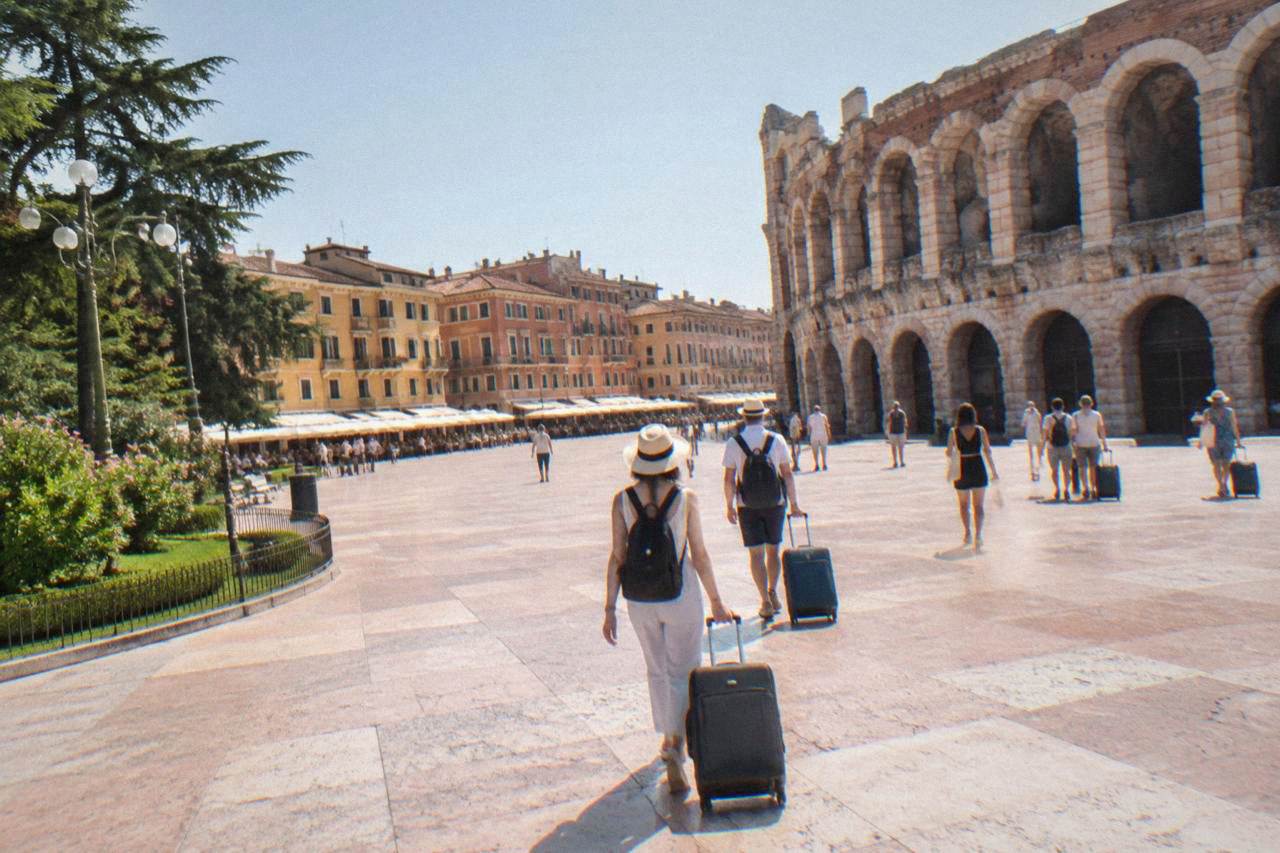 Travellers with suitcases walking across Piazza Bra in Verona toward the Arena amphitheatre