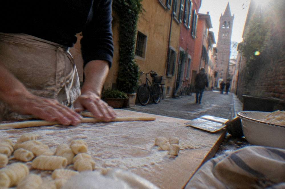 Hands rolling potato gnocchi dough on a floured wooden board