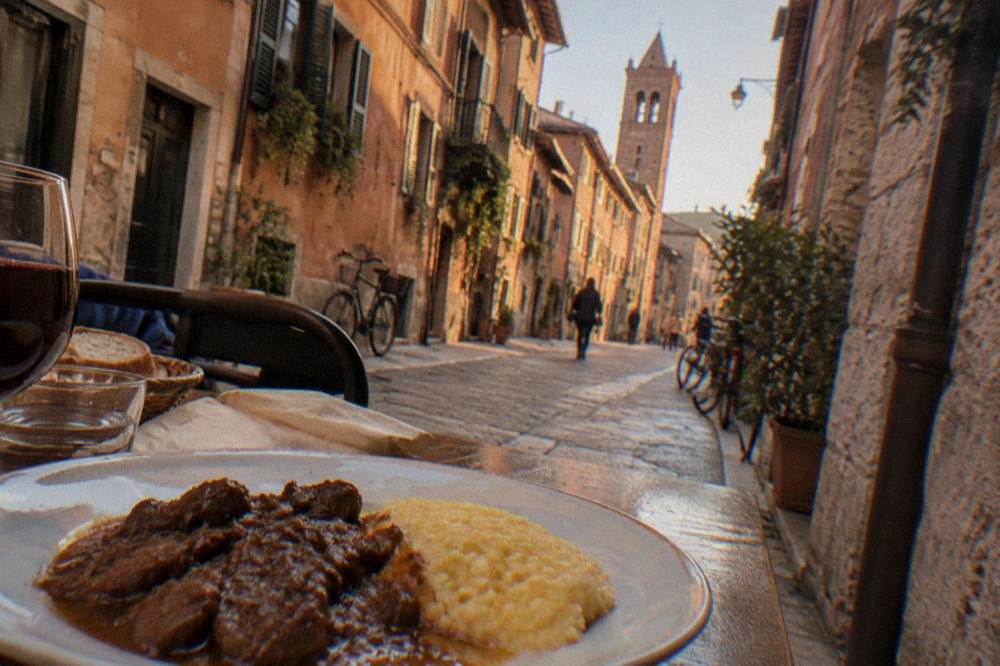 Bowl of slow-cooked stew beside polenta on a plain plate, no labels
