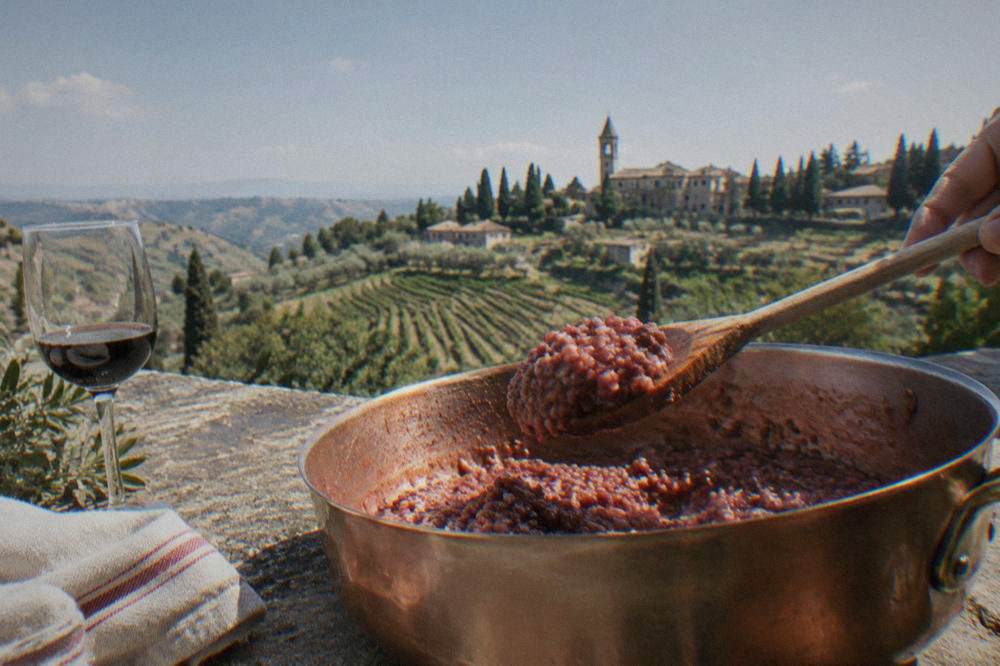A wooden spoon lifting creamy red risotto from a copper pan