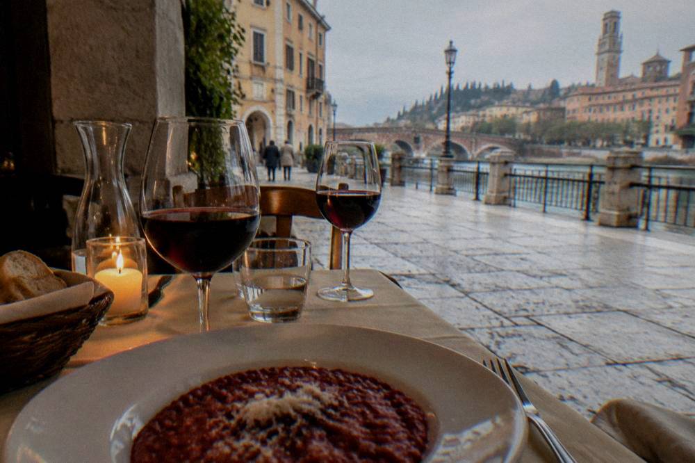 A candlelit trattoria table in Verona with wine glasses and a plate of red risotto
