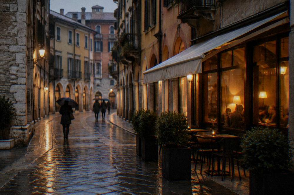 A rainy evening street in Verona with warm light from a restaurant window