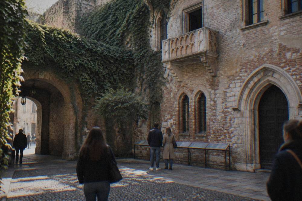 A bronze statue of a young woman standing in a stone courtyard surrounded by visitors