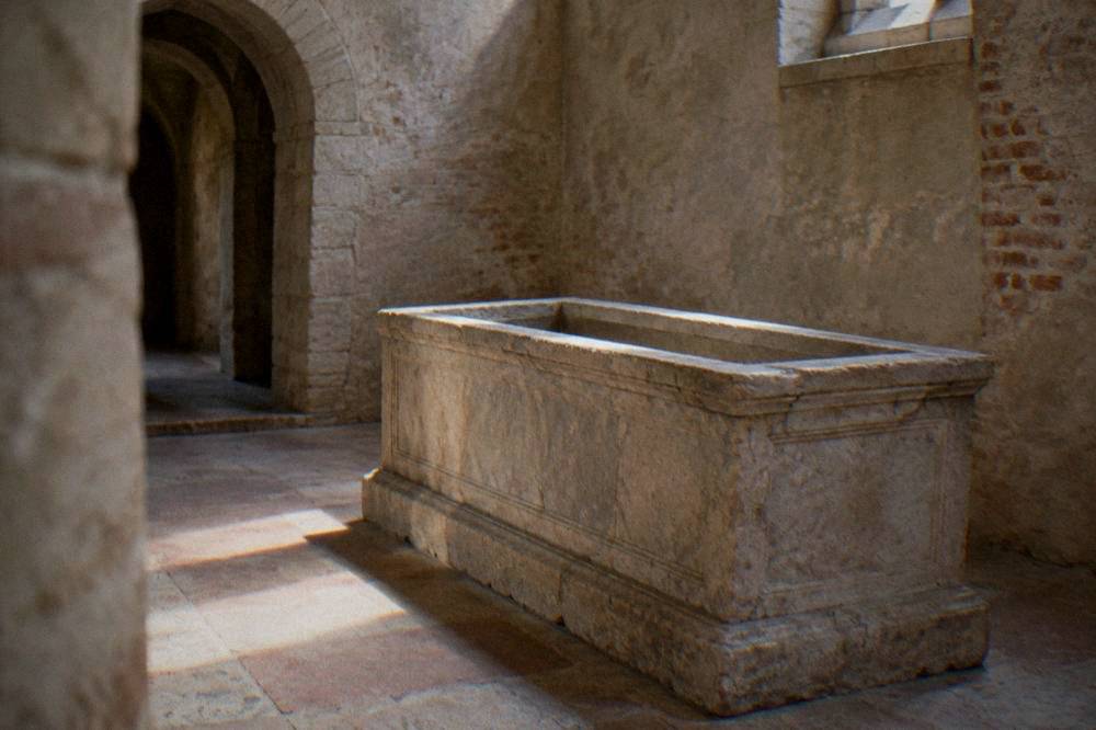 A plain stone chamber with an empty open sarcophagus lit softly from above