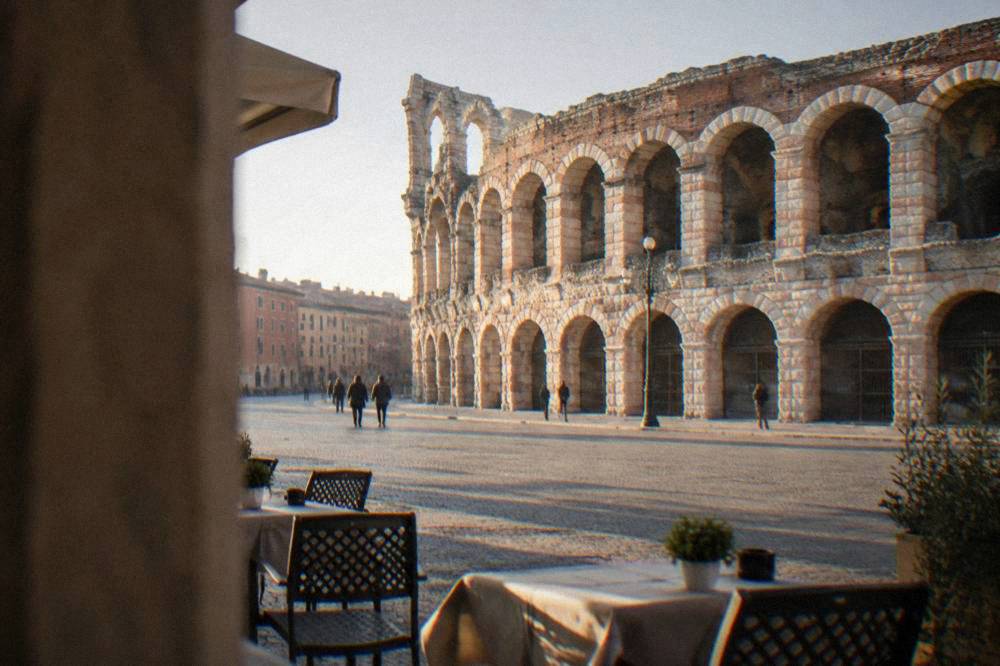 The pink marble Arena rising at the edge of Piazza Bra with cafe tables in the foreground