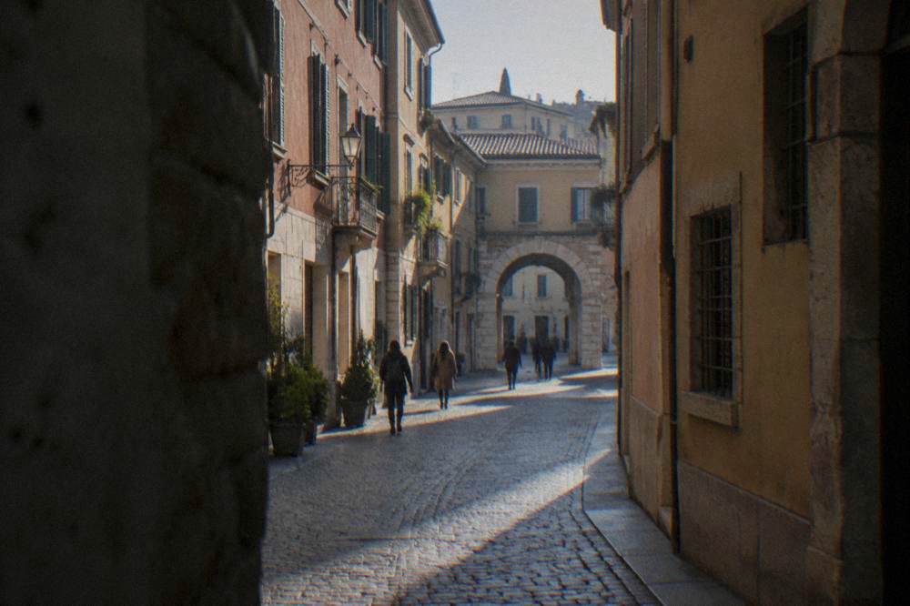 A narrow cobbled street in central Verona with pastel buildings and a stone archway