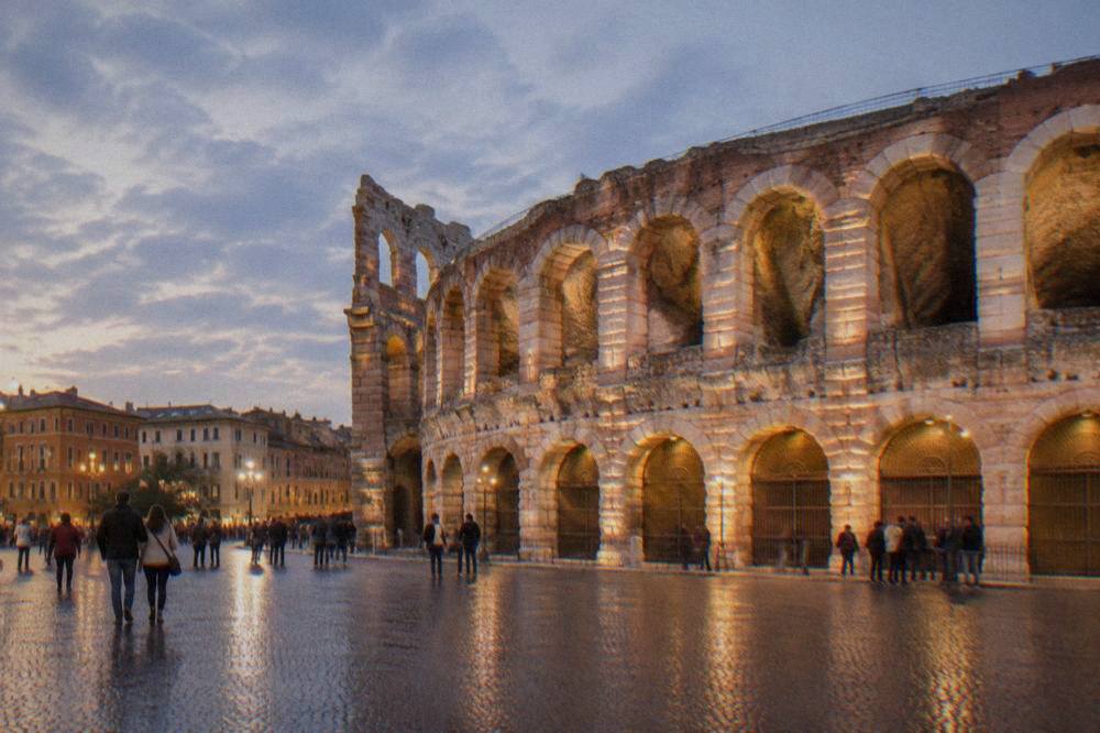 The Arena lit by evening floodlight with people gathered on the square outside