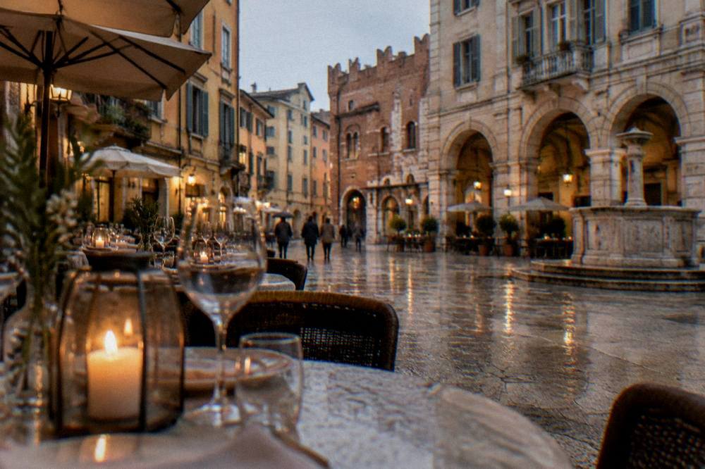 Candlelit tables set for dinner outside a restaurant on a Verona square