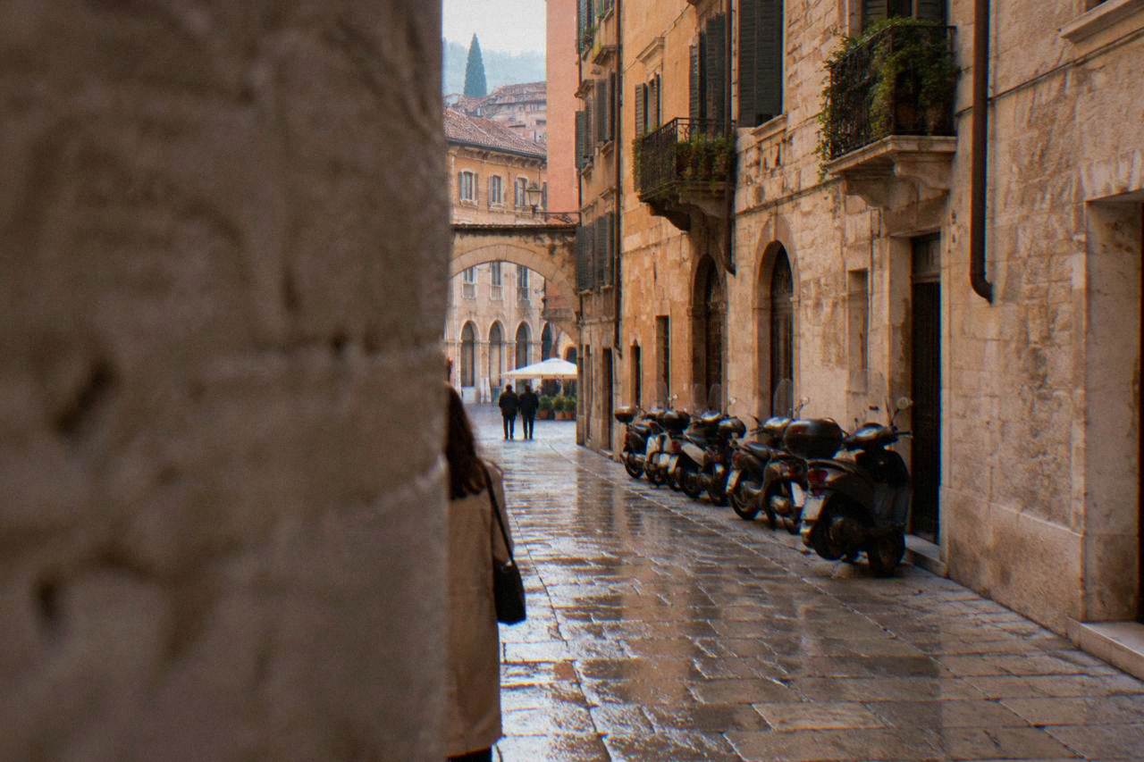 A narrow Verona street with stone buildings and parked scooters along the edge