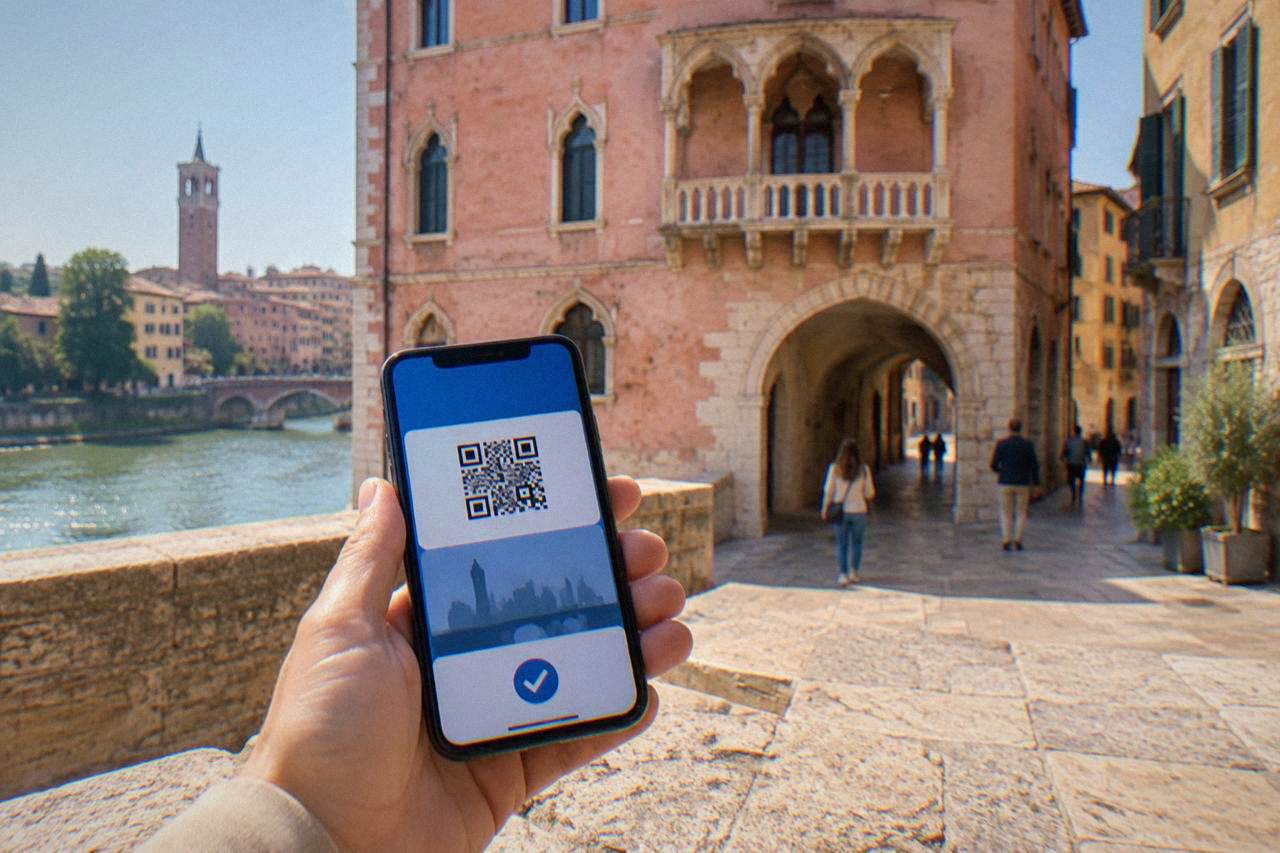 A visitor holding a smartphone showing a digital city pass in front of a rose-pink medieval building in Verona