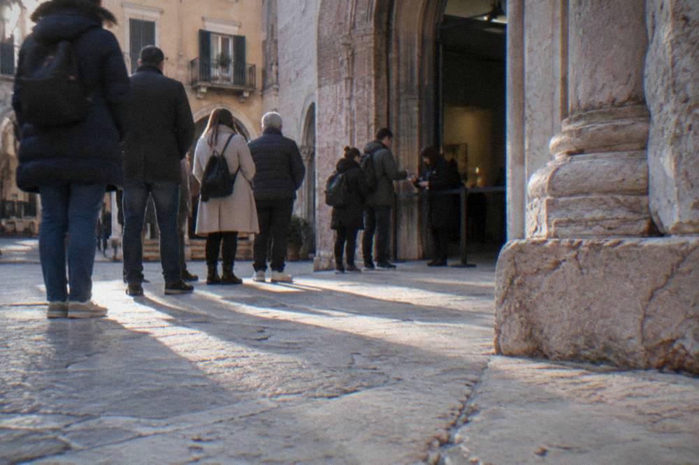 Tourists queuing at a museum entrance in central Verona with a staff member scanning a phone screen
