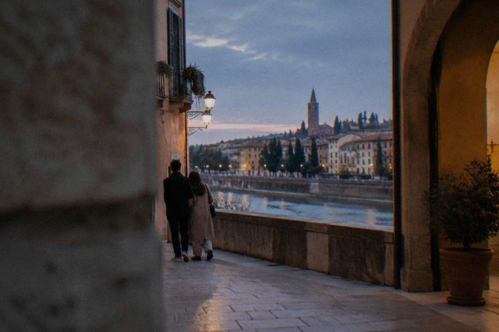 A couple comparing a phone screen with a paper map at a sunlit square in Verona