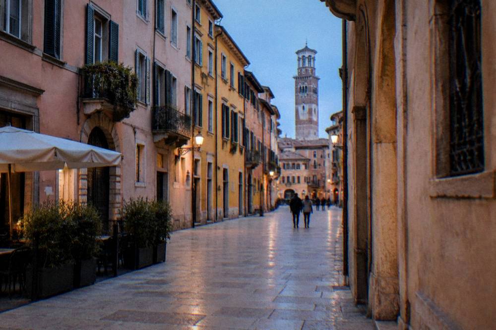 A street in central Verona with marble pavements and pastel facades leading toward a tower