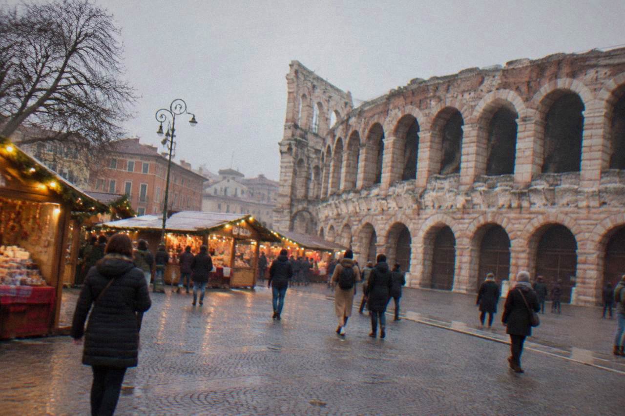 Christmas market stalls with warm lights standing in a wide Verona square beside an old Roman amphitheatre