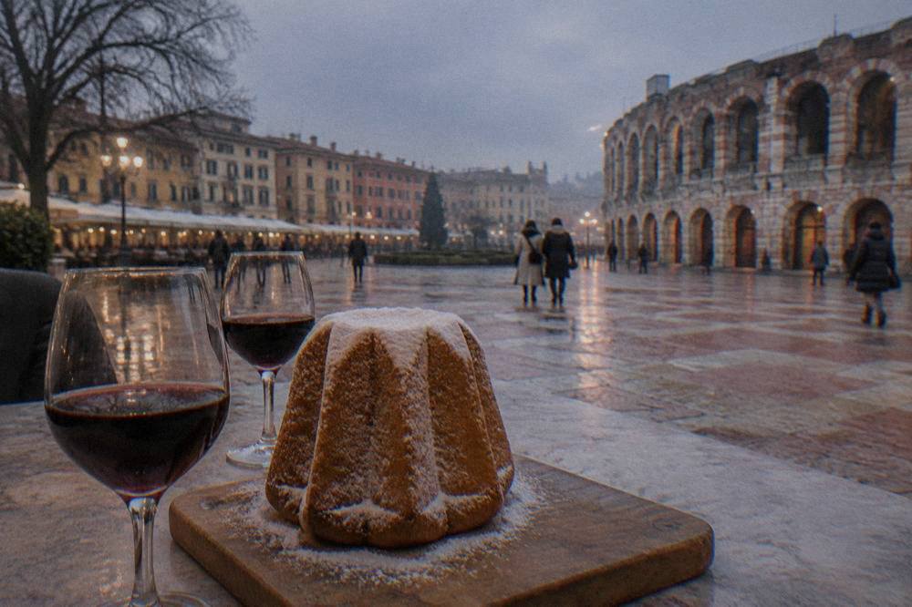A star-shaped golden pandoro cake dusted with sugar on a wooden board beside two glasses of red wine