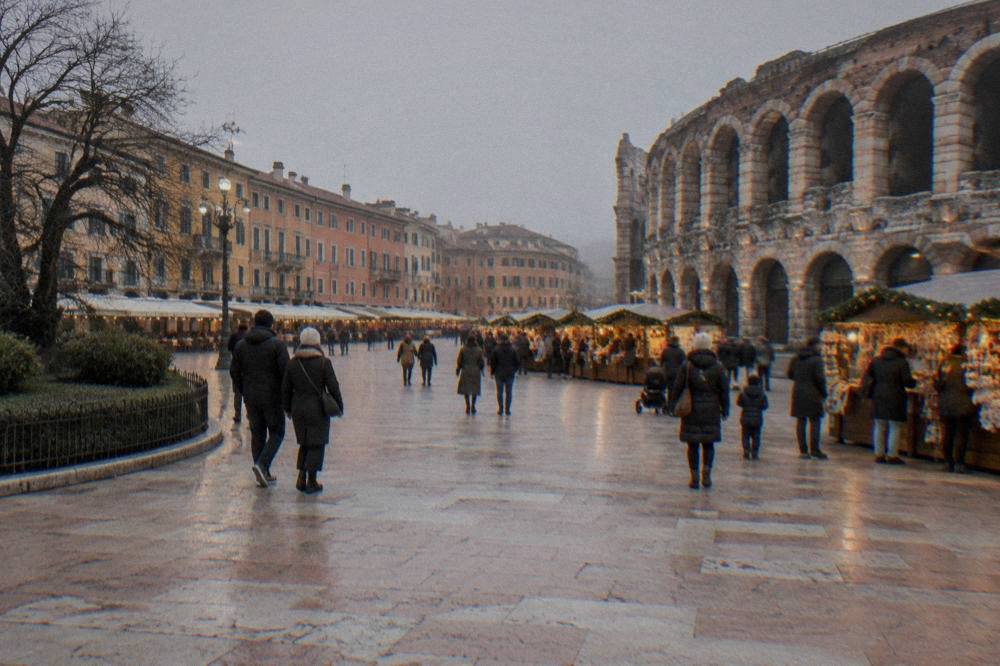 Families and couples browsing wooden market stalls hung with lights in the early evening in an Italian square