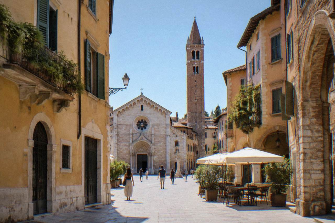 A stone church facade with a tall bell tower rising above a narrow Verona street