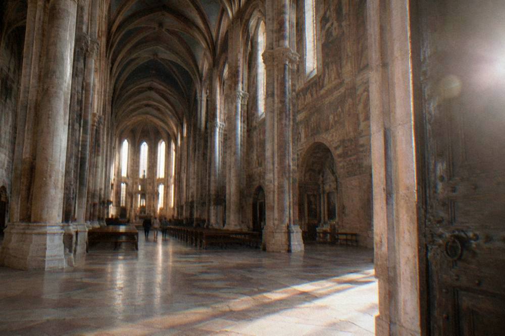 A wide painted church nave with tall columns and frescoed walls seen from the entrance