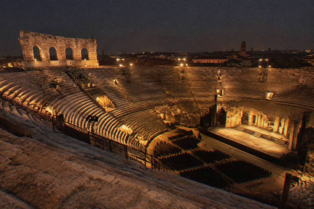 The illuminated interior of the Arena di Verona seen from the upper stone tiers at night