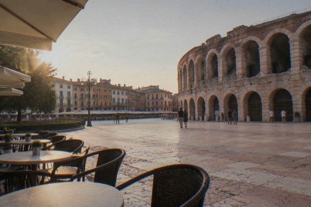 A wide view of Piazza Bra in Verona with the Arena's facade on one side and cafe tables in the foreground