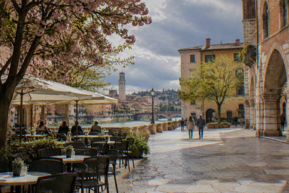 Café tables set out on a Verona square under spring blossom