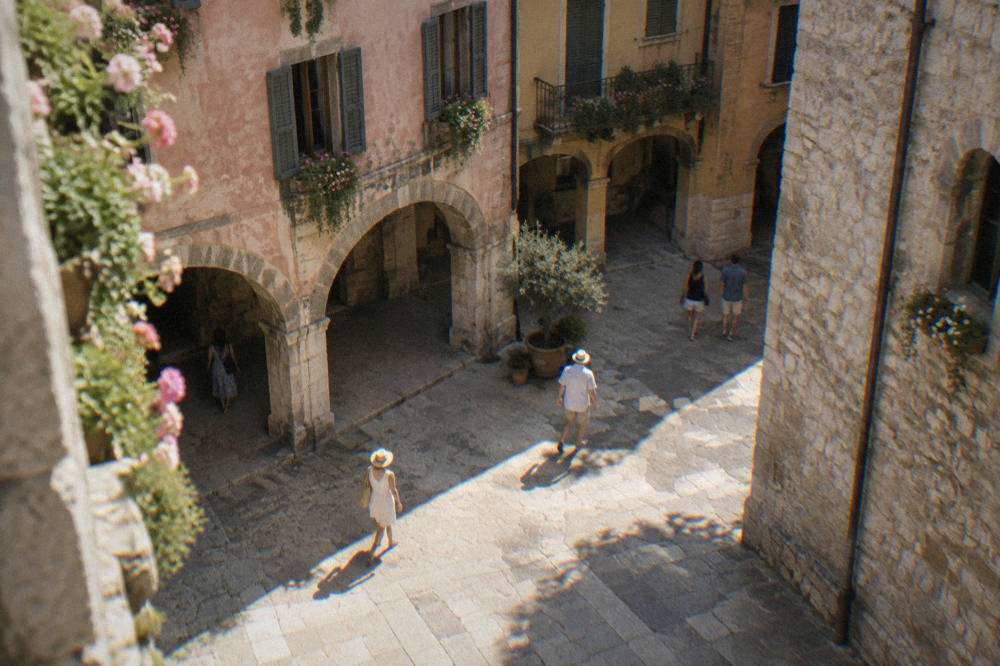 A shaded medieval courtyard in Verona with stone walls and hanging flower boxes on a bright afternoon