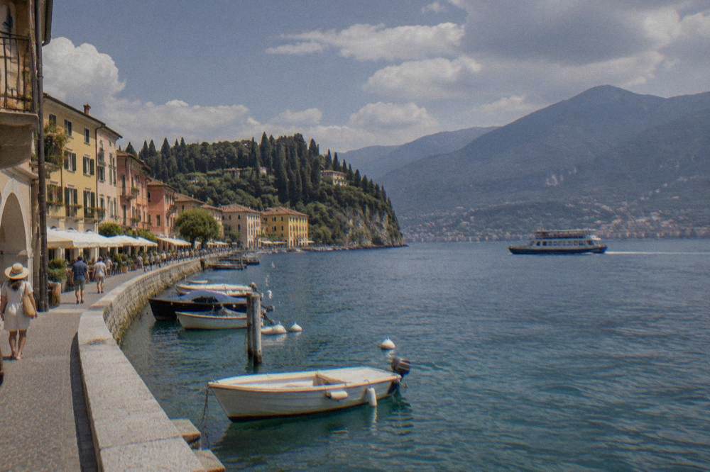A ferry crossing open water on Lake Garda towards a lakeside town with hills behind