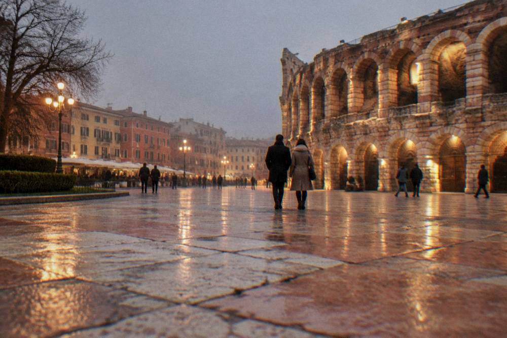 A coat-wearing couple walking across Piazza Bra toward the lit Arena at night