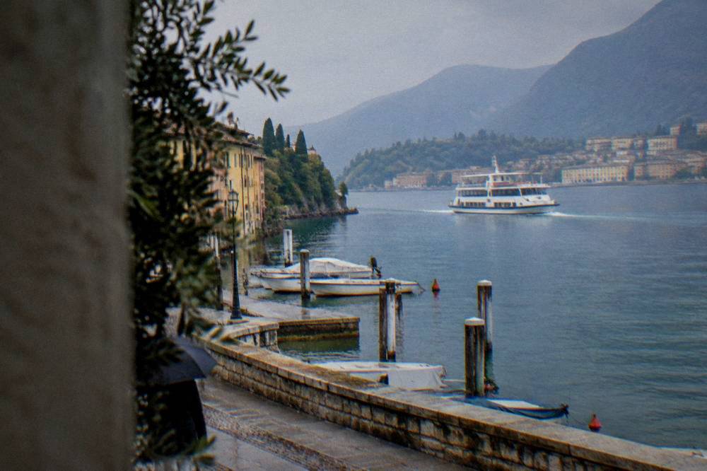 A white Lake Garda ferry crossing open water towards a lakeside town with hills behind