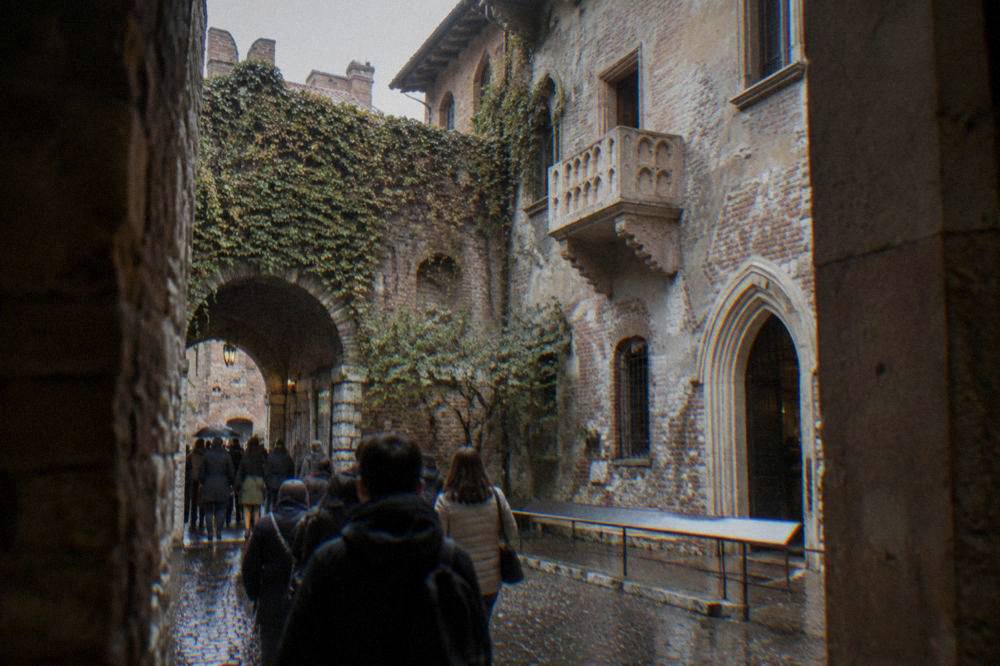 Visitors with tickets entering Juliet's courtyard in Verona past the stone walls and the famous balcony above