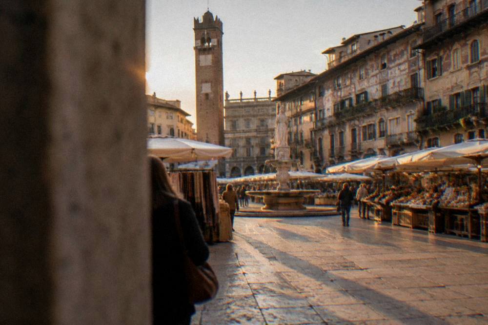 Piazza delle Erbe in Verona at golden hour with its market stalls, frescoed buildings and the tower above